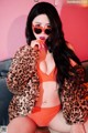 A woman in a leopard print jacket and orange bikini sitting on a couch.