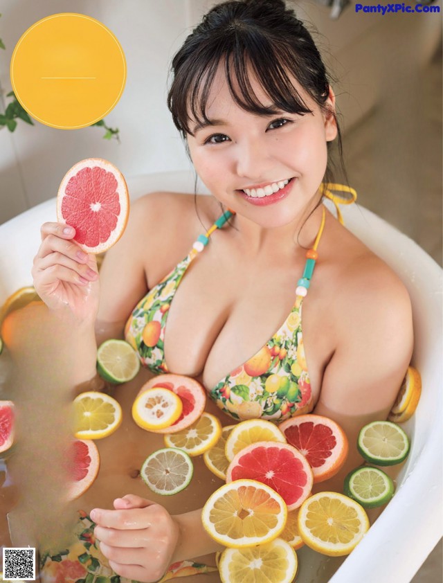 A woman in a bathtub holding a slice of grapefruit.