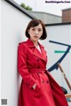 a woman in a red coat leaning against a wall