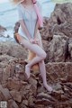 A woman with pink hair sitting on a rock by the ocean.